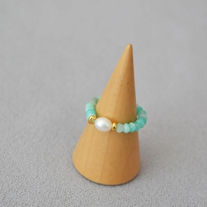 Close-up of amazonite beads ring with a central pearl and gold spacers on wood stand