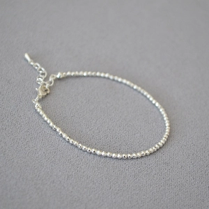 Detail of silver faceted beads necklace with adjustable lobster clasp on grey fabric