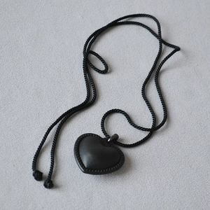 Détail macro d'un pendentif cœur noir 3D avec texture cuir cousue et cordon torsadé