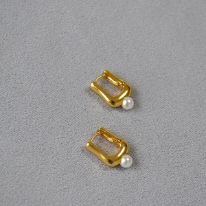 Gros plan sur les boucles d'oreilles dorées en forme de U avec perles blanches et fermoir