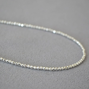Macro shot of silver beaded necklace with fine faceted cut beads on dark fabric