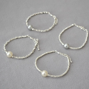 Detailed close-up of beaded irregular silver bracelets with white and grey pearls