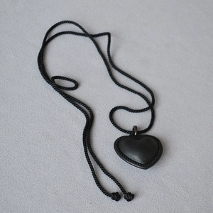 Détail d'un pendentif cœur en cuir noir avec bordures cousues et chaîne en corde torsadée