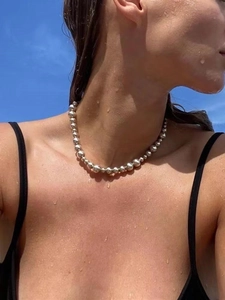 Close-up of silver-gray gradient pearl necklace worn by a model on a blue sky background