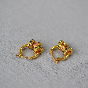 Détail de créoles dorées avec des breloques amovibles en zircon rouge, vert et bleu