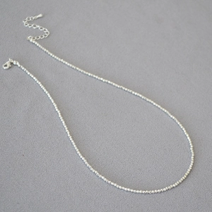 Macro detail of silver beaded necklace with faceted metallic beads and lobster clasp