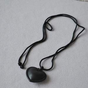 Détail macro du pendentif coeur en cuir noir avec cordon tressé et surpiqûres