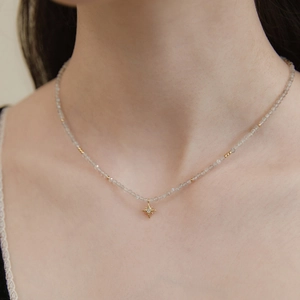 Detail of beaded moonstone necklace featuring a gold starburst pendant on model neck