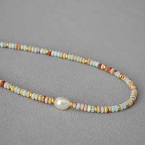 Close-up of a beaded necklace with baroque pearl, blue stones, and golden spacers