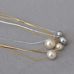 Detailed view of layered gold and silver pearl necklaces on light gray fabric texture