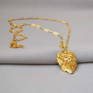 Detail of golden lion head pendant with red gemstone eyes on a textured chain
