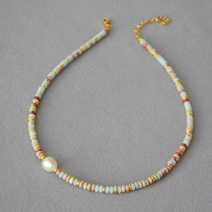 Detail of beaded necklace with blue and red stones, large white pearl and gold clasp