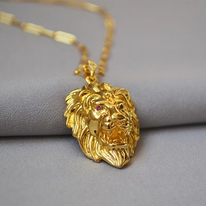 Detailed macro shot of a golden lion head pendant with red gemstone eyes on a chain