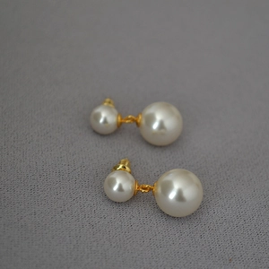 Detail of elegant double pearl stud earrings with gold plating on a textured background