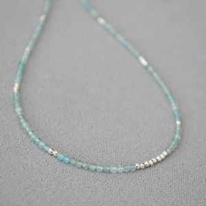 Macro detail of minimalist aquamarine beaded necklace with silver accents on grey fabric