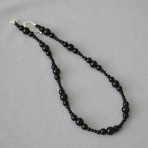Elegant beaded necklace with black onyx stones and silver lobster clasp on grey fabric