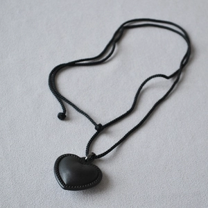 Détail d'un pendentif cœur en cuir noir avec bordure métallique tressée sur un cordon