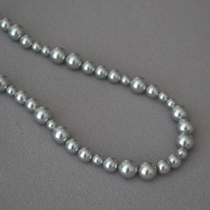 Macro detail of gray irregular pearl necklace with alternating sizes on textured fabric