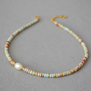 Detail of beaded necklace with blue stones, gold spacers, and a white pearl accent