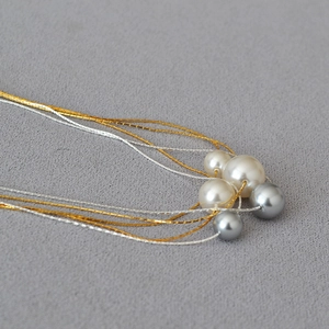 Detailed close-up of layered gold wire necklace with white and grey faux pearls