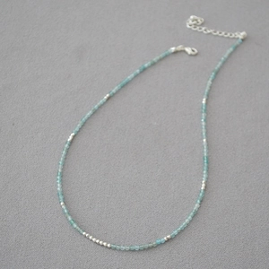 Detail of beaded necklace with blue-green stones and silver spacer beads on grey background