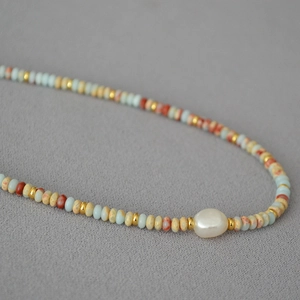 Detailed shot of beaded necklace with blue stones, golden spacers and a baroque pearl