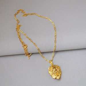 Detail of golden lion head pendant with red eye accents and chunky paperclip chain link