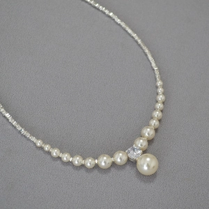 Macro detail of high-luster faux pearl necklace with silver bead accents and zircon pendant