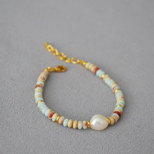 Macro detail of beaded necklace with blue spotted stones, pearl, and gold lobster clasp