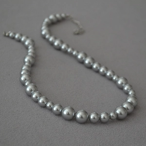 Macro detail of metallic grey pearl necklace with gradient sizing on grey fabric background