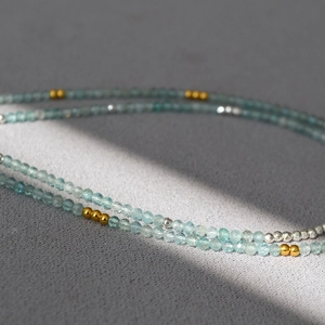 Detailed macro view of a 2mm blue-green apatite stone necklace with gold spacer beads