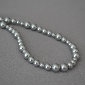 Macro shot of silver-grey faux pearl necklace with alternating bead sizes on fabric