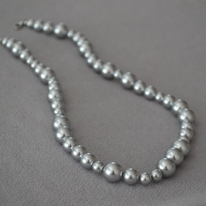 Detailed view of silver grey gradient pearl necklace on grey textured fabric background