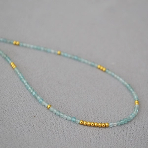 Detail of slim aquamarine beaded necklace with polished gold metal spacers on gray fabric