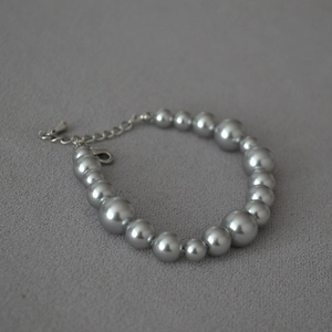 Detail of silver grey pearl bracelet with graduated sizes and silver lobster clasp on fabric