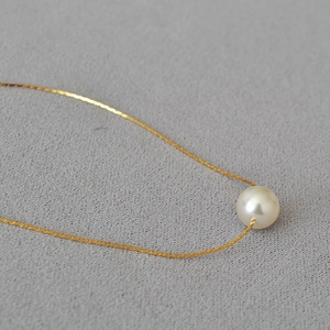 Macro shot of minimalist gold necklace with a glossy single pearl pendant detail
