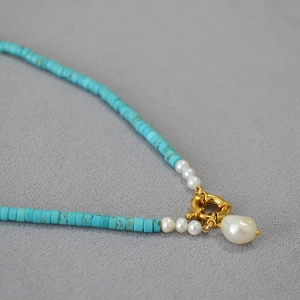 Macro detail of turquoise bead necklace with irregular baroque pearl pendant and gold clasp