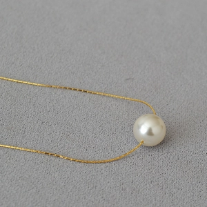 Detail of 10mm round pearl pendant on a delicate gold chain over grey textured fabric