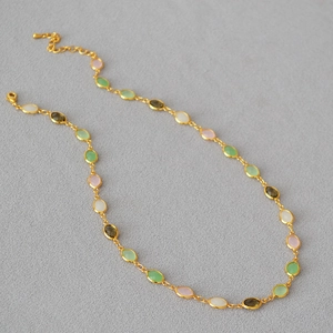 Close-up of a gold necklace featuring colorful oval gems and an adjustable metal chain
