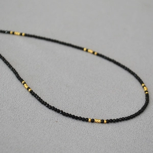 Elegante dünne schwarze Spinell-Halskette mit Goldakzenten auf grauem Stoffhintergrund