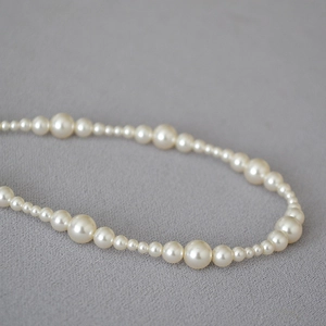 Detailed close-up of gradient cream pearls on a beaded necklace with unique alternating sizes