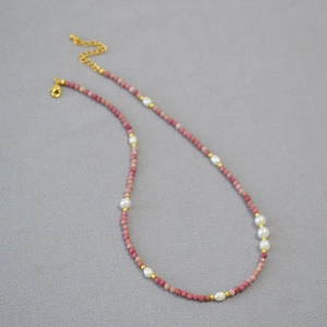 Pink gemstone beaded necklace with freshwater pearls and adjustable gold clasp on gray fabric