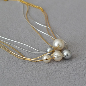 Macro detail of multi-layer gold and silver chains with five elegant white and grey pearls