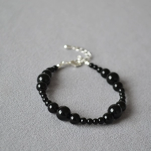 Detail of beaded black onyx bracelet with silver lobster clasp on grey fabric background