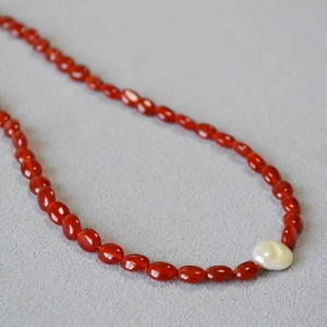 Détail du collier de perles en agate rouge avec une perle baroque blanche centrale