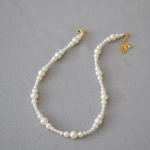 Detail of white pearl necklace with gradient sizing and golden lobster clasp closure