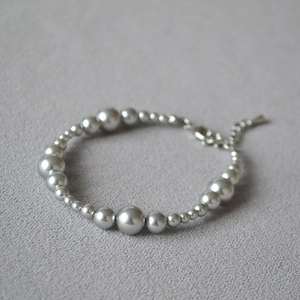 Macro shot of grey pearl bracelet with silver lobster clasp on a textured stone surface