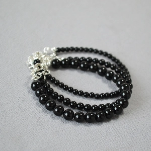 Three-layer black beaded bracelet with silver metal clasp on a textured background