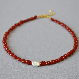 Détail d'un collier en perles d'agate rouge avec une perle baroque blanche au centre