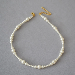 Detail of white pearl necklace with gold lobster clasp on textured grey background
